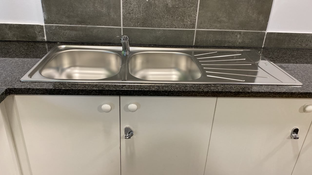 Stainless steel double bowl kitchen sink with drainer and mixer tap on a granite top