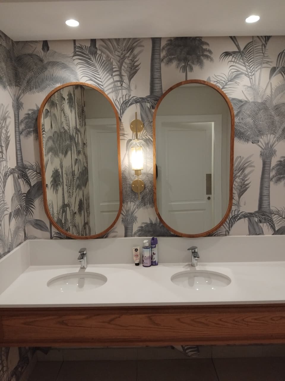 Twin undermount basins on a solid surface countertop beneath two oval mirrors